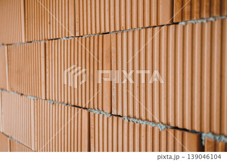 Brick wall construction showing orange bricks stacked with mortar, indicating building work taking place in an urban setting during daylight hours Brick wall construction showing orange bricks stacked with mortar, indicating building work taking place in an urban setting during daylight hours 139046104
