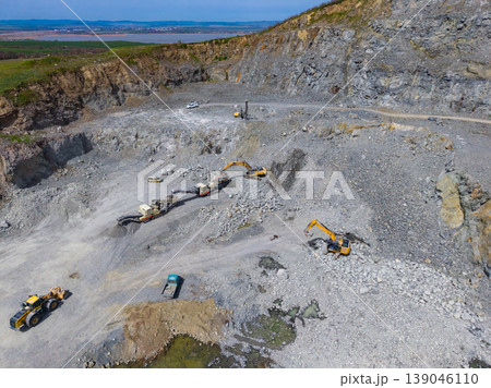 Granite quarry with large machines working on stone extraction in a remote area during a clear day Granite quarry with large machines working on stone extraction in a remote area during a clear day 139046110