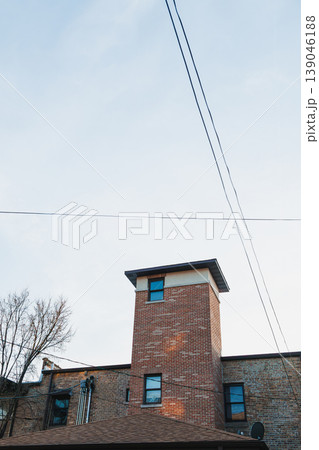 View of a brick building with a tower and clear sky during the day in an urban area, showcasing the architecture and nearby trees and power lines View of a brick building with a tower and clear sky during the day in an urban area, showcasing the architecture and nearby trees and power lines 139046188