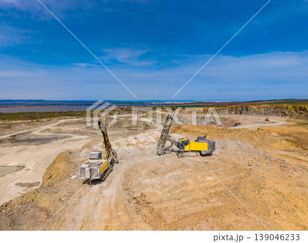 Granite quarry activity with heavy machinery working under a clear blue sky near a large water body in a remote area Granite quarry activity with heavy machinery working under a clear blue sky near a large water body in a remote area 139046233
