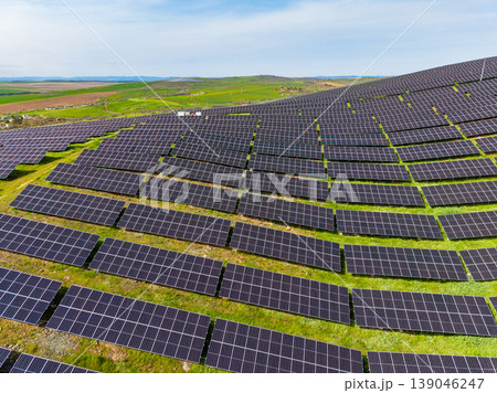 Solar panels line a large field in an open area with green hills in the background on a clear day with blue sky Solar panels line a large field in an open area with green hills in the background on a clear day with blue sky 139046247