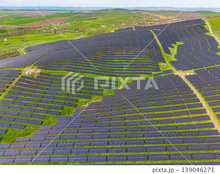 Large solar farm covers a hillside with rows of solar panels in a rural area during daytime with green fields in the background and clear skies above Large solar farm covers a hillside with rows of solar panels in a rural area during daytime with green fields in the background and clear skies above 139046271