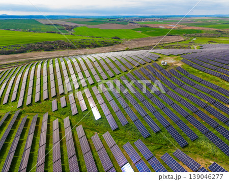 Solar panels cover a large area of land in a rural setting with green fields in the background during a cloudy day with distant hills 139046277