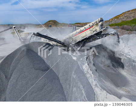 Granite quarry operation with machines processing stone and creating dust in an open area during daylight hours 139046305