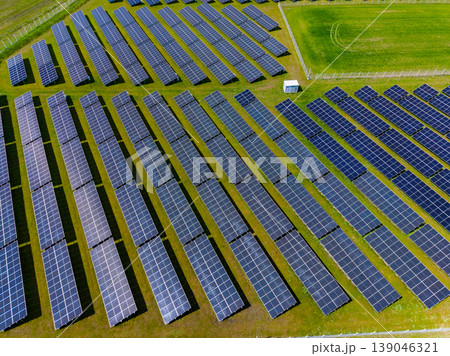Large solar panel installation in a green field under bright sunlight with clear skies, showing rows of panels organized systematically for energy generation Large solar panel installation in a green field under bright sunlight with clear skies, showing rows of panels organized systematically for energy generation 139046321