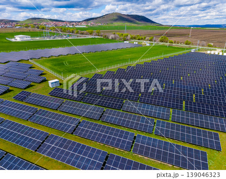 Solar panels cover land in a renewable energy farm located in a rural area with hills in the background during daytime under clouds 139046323