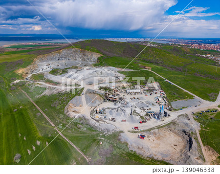Granite quarry located near a green hillside and a distant city with visible clouds in the sky 139046338