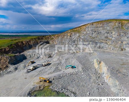 Granite quarry site showing extraction activities, heavy machinery, and large stone blocks near a hill with a cloudy sky 139046404
