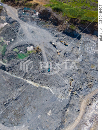 Granite quarry with heavy machinery and rocky terrain in daytime under clear sky and green hills in the background Granite quarry with heavy machinery and rocky terrain in daytime under clear sky and green hills in the background 139046407