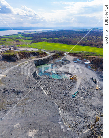 Workers are extracting granite at a large granite quarry located near a body of water and surrounded by green fields 139046414