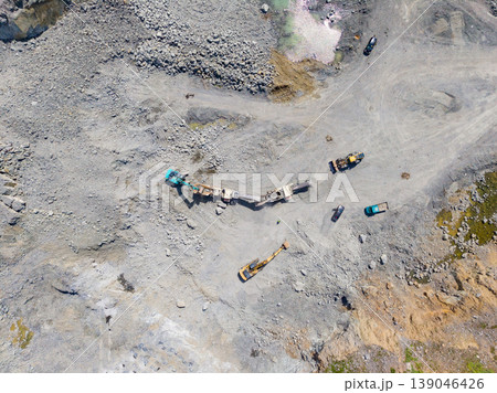 Workers operate heavy machinery in a granite quarry with multiple machines involved in stone extraction and transportation 139046426