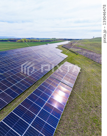 Solar panels cover a large area in a green field under bright skies during daytime near a rural location in an open landscape Solar panels cover a large area in a green field under bright skies during daytime near a rural location in an open landscape 139046478