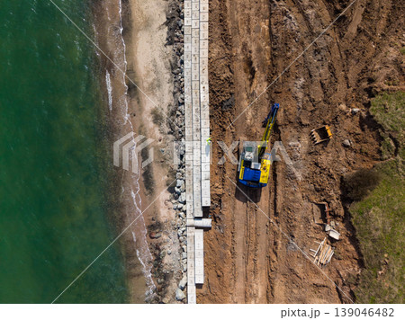 Construction of concrete structures along a beach at low tide with construction equipment and materials present on the ground 139046482