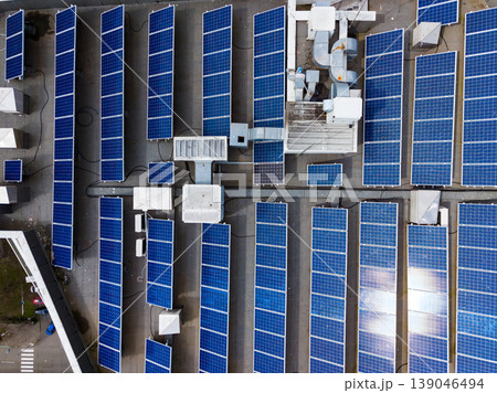 Solar panels cover a large rooftop on a building during daylight hours, showing the arrangement of the panels and surrounding equipment Solar panels cover a large rooftop on a building during daylight hours, showing the arrangement of the panels and surrounding equipment 139046494
