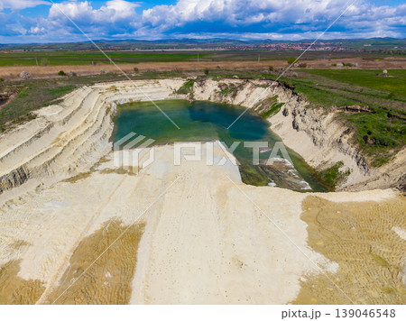 Large sandy pit with water in the center located in an open area surrounded by fields and blue skies with clouds Large sandy pit with water in the center located in an open area surrounded by fields and blue skies with clouds 139046548