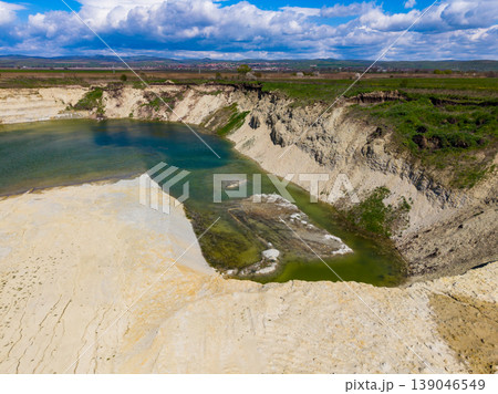 Clouds float above a water-filled pit in a landscape with grass, sand, and rocky edges in a rural area during daytime Clouds float above a water-filled pit in a landscape with grass, sand, and rocky edges in a rural area during daytime 139046549