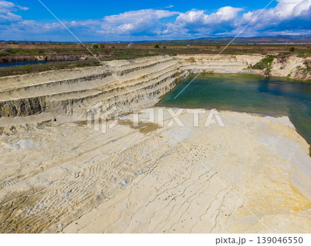Large industrial site shows steep sandy cliffs and green water pool near flat land, under bright blue sky with some clouds during day Large industrial site shows steep sandy cliffs and green water pool near flat land, under bright blue sky with some clouds during day 139046550