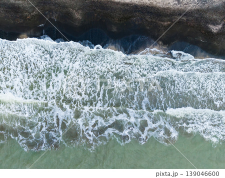 Waves crash on the shore as water flows over sand during daytime on a coastline with dark and light tones Waves crash on the shore as water flows over sand during daytime on a coastline with dark and light tones 139046600