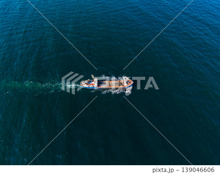Large cargo ship moves through deep blue water in the ocean during the day while leaving a small wake behind Large cargo ship moves through deep blue water in the ocean during the day while leaving a small wake behind 139046606