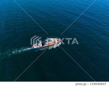 View of a cargo ship sailing over the wide blue ocean during daytime while leaving a wake of white foam behind in the clear waters View of a cargo ship sailing over the wide blue ocean during daytime while leaving a wake of white foam behind in the clear waters 139046607