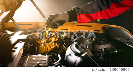 Mechanic checking engine oil level with dipstick in car engine. Automotive maintenance, inspection and professional service concept in workshop. Mechanic checking engine oil level with dipstick in car engine. Automotive maintenance, inspection and professional service concept in workshop. 139046909