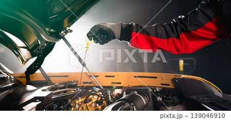 Mechanic checking engine oil level with dipstick in car engine. Automotive maintenance, inspection and professional service concept in workshop. Mechanic checking engine oil level with dipstick in car engine. Automotive maintenance, inspection and professional service concept in workshop. 139046910