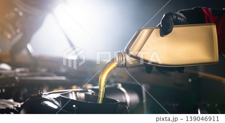 Mechanic pouring engine oil into car engine in workshop. Automotive maintenance, oil change service and professional repair concept with dramatic lighting. Mechanic pouring engine oil into car engine in workshop. Automotive maintenance, oil change service and professional repair concept with dramatic lighting. 139046911