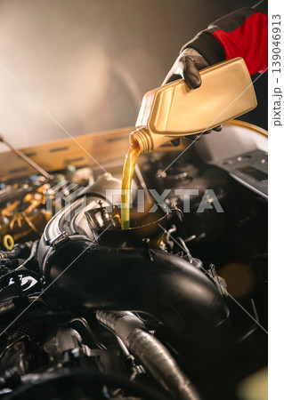 Mechanic pouring engine oil into car engine in workshop. Automotive maintenance, oil change service and professional repair concept with dramatic lighting. 139046913