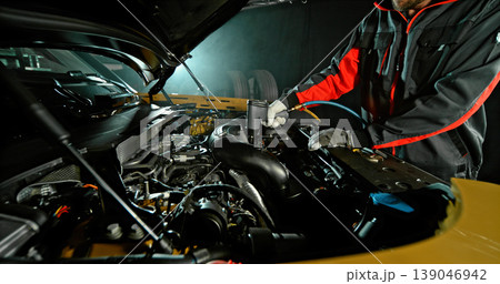 Mechanic repairing car engine in workshop, using tools with dramatic lighting. Automotive maintenance and professional service concept. 139046942