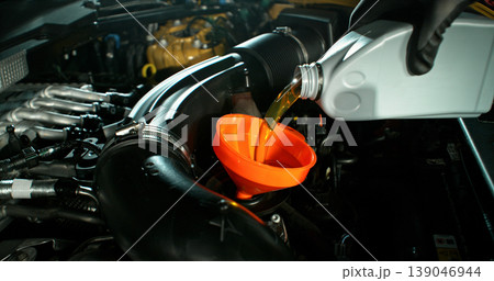 Mechanic pouring engine oil into car engine in workshop. Automotive maintenance, oil change service and professional repair concept with dramatic lighting. Mechanic pouring engine oil into car engine in workshop. Automotive maintenance, oil change service and professional repair concept with dramatic lighting. 139046944