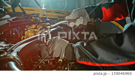 Mechanic repairing car engine in workshop, using tools with dramatic lighting. Automotive maintenance and professional service concept. Mechanic repairing car engine in workshop, using tools with dramatic lighting. Automotive maintenance and professional service concept. 139046960