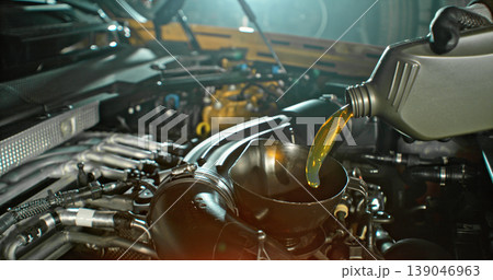 Mechanic pouring engine oil into car engine in workshop. Automotive maintenance, oil change service and professional repair concept with dramatic lighting. Mechanic pouring engine oil into car engine in workshop. Automotive maintenance, oil change service and professional repair concept with dramatic lighting. 139046963
