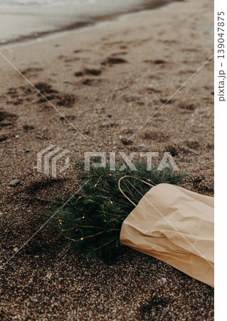 Craft Bag with Spruce branches with Christmas lights laying on a sand on the beach. 139047875