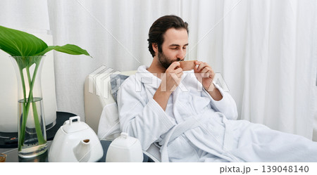 Portrait of handsome man in white bathrobe drinking healing tea while relaxing in wellness center. Men spa program Portrait of handsome man in white bathrobe drinking healing tea while relaxing in wellness center. Men spa program 139048140