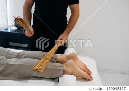 Bamboo brooms in masseur hands in motion while massaging legs of massage parlor patient. Massage with bamboo sticks Bamboo brooms in masseur hands in motion while massaging legs of massage parlor patient. Massage with bamboo sticks 139048167