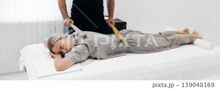 Samurai massage with bamboo brooms for female body at wellness center with massage therapist. Rhythmic shock-resonance massage using bamboo brooms and sticks Samurai massage with bamboo brooms for female body at wellness center with massage therapist. Rhythmic shock-resonance massage using bamboo brooms and sticks 139048169
