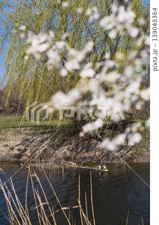 Ducks relaxing in a pond, a spring willow, and blooming cherry plums over a canal, a vertical poster about spring and a weekend getaway in nature Ducks relaxing in a pond, a spring willow, and blooming cherry plums over a canal, a vertical poster about spring and a weekend getaway in nature 139048364