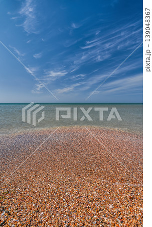 shell beach and a calm, clear sea, copy space. A concept for advertising a vacation on the magnificent beaches of the Mediterranean, a sky with wispy clouds shell beach and a calm, clear sea, copy space. A concept for advertising a vacation on the magnificent beaches of the Mediterranean, a sky with wispy clouds 139048367