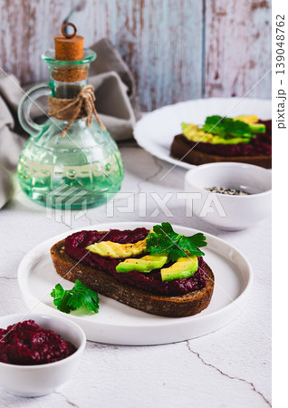 Beetroot hummus and avocado on rye bread on a plate on the table vertical view 139048762