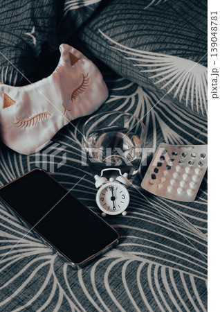 Insomnia medication, water, a smartphone, and a mask on the bed vertical view Insomnia medication, water, a smartphone, and a mask on the bed vertical view 139048781