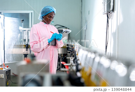 African American woman factory worker write the detail and check follow the standard checklists on document file for the quality of product in the bottle in line productivity in drinking industrial 139048844