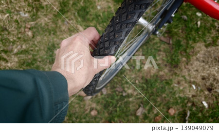 Hand checking the tire of a red bicycle on the grass outdoors Hand checking the tire of a red bicycle on the grass outdoors 139049079