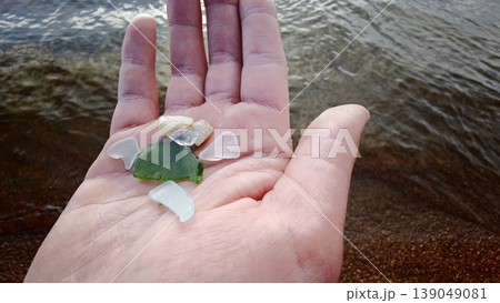 Hand holding pieces of sea glass on a beach near water on a sunny day 139049081