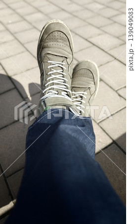 Person sits with legs crossed and shoes on pavement in a sunny setting 139049083