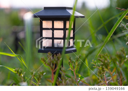 Contemporary solar LED garden lantern, flower border with perennial grasses, mulch and stone, low-maintenance eco planting, modern design. 139049166