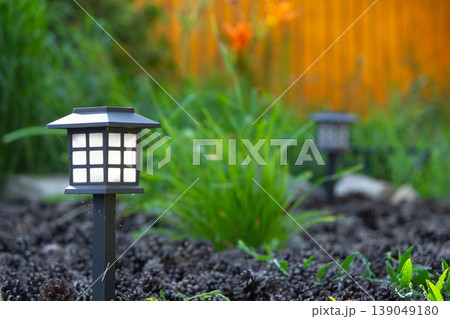Modern solar garden lantern, mulch and daylily flowerbed, ornamental grass accents, eco-friendly design, contemporary night LED path lighting, perennial combo. Modern solar garden lantern, mulch and daylily flowerbed, ornamental grass accents, eco-friendly design, contemporary night LED path lighting, perennial combo. 139049180