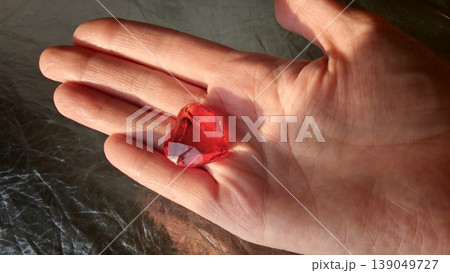 Hand holds a red heart-shaped gem on a reflective surface during sunset Hand holds a red heart-shaped gem on a reflective surface during sunset 139049727
