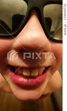 Smiling child with glasses showing teeth in a close-up view at home 139049728