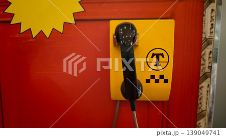 Bright yellow taxi phone on red wall in a busy urban area during the day 139049741