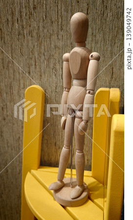 Wooden mannequin stands on yellow chair in studio or workspace during daytime 139049742